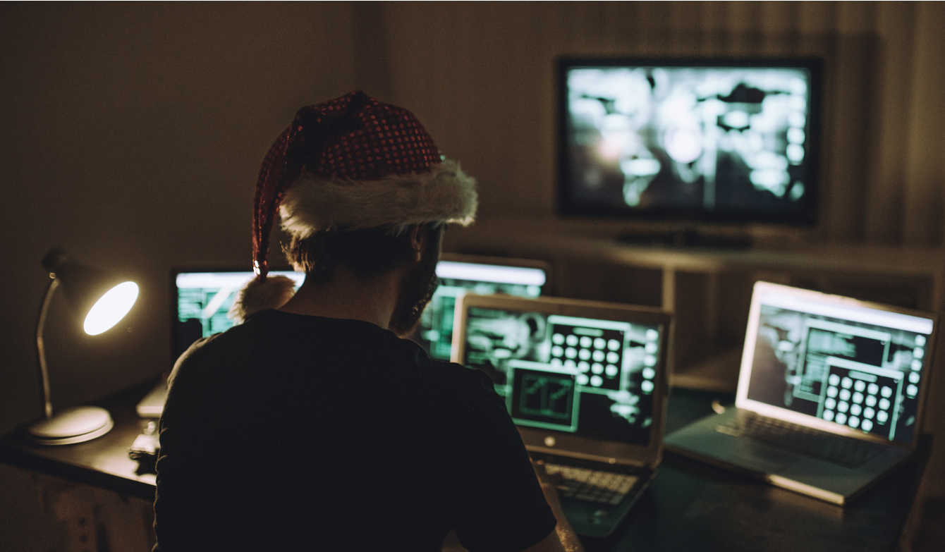 Computer hacker wearing Santa hat while working on laptop late at night.