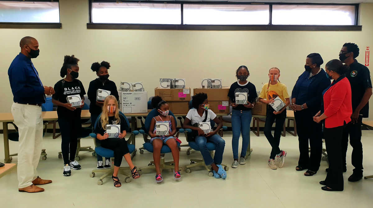 From l2r back: Pedro Parilla receives headphones from Makayla Walcott, Nialah Addison, Jade Browne, Vigga Tyson. L to R (seated): Norma Tyson, Jaylissa Browne and Zuma Nesbitt. Far Right: Jeselle Cruse-Peter, Dr. Everette Ryan, Paulina Croskey