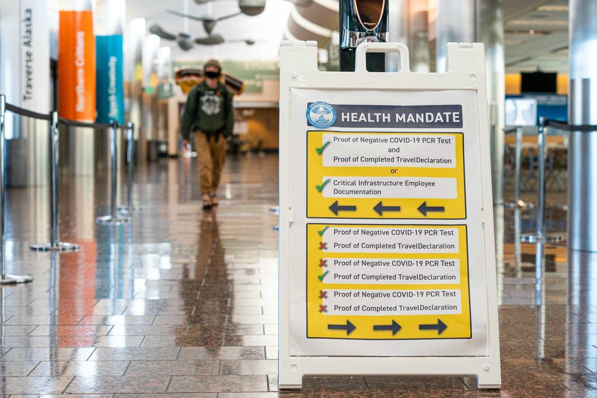A person walks past a sign explaining a new state health mandate requiring COVID-19 testing for travelers entering Alaska on Friday, June 5, 2020 at the Ted Stevens Anchorage International Airport.