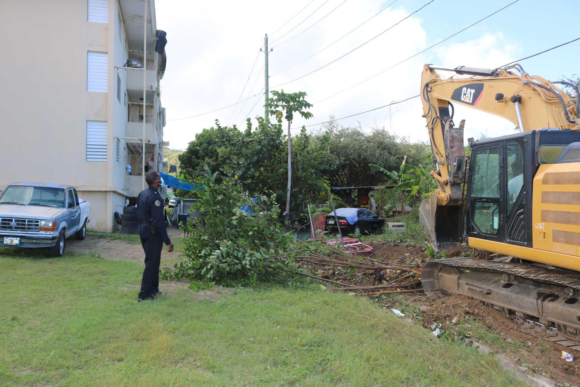 St. Croix District Deputy Police Chief Uston Cornelius looks on as heavy equipment is used to clean the area behind of the John F. Kennedy Terrace housing community.