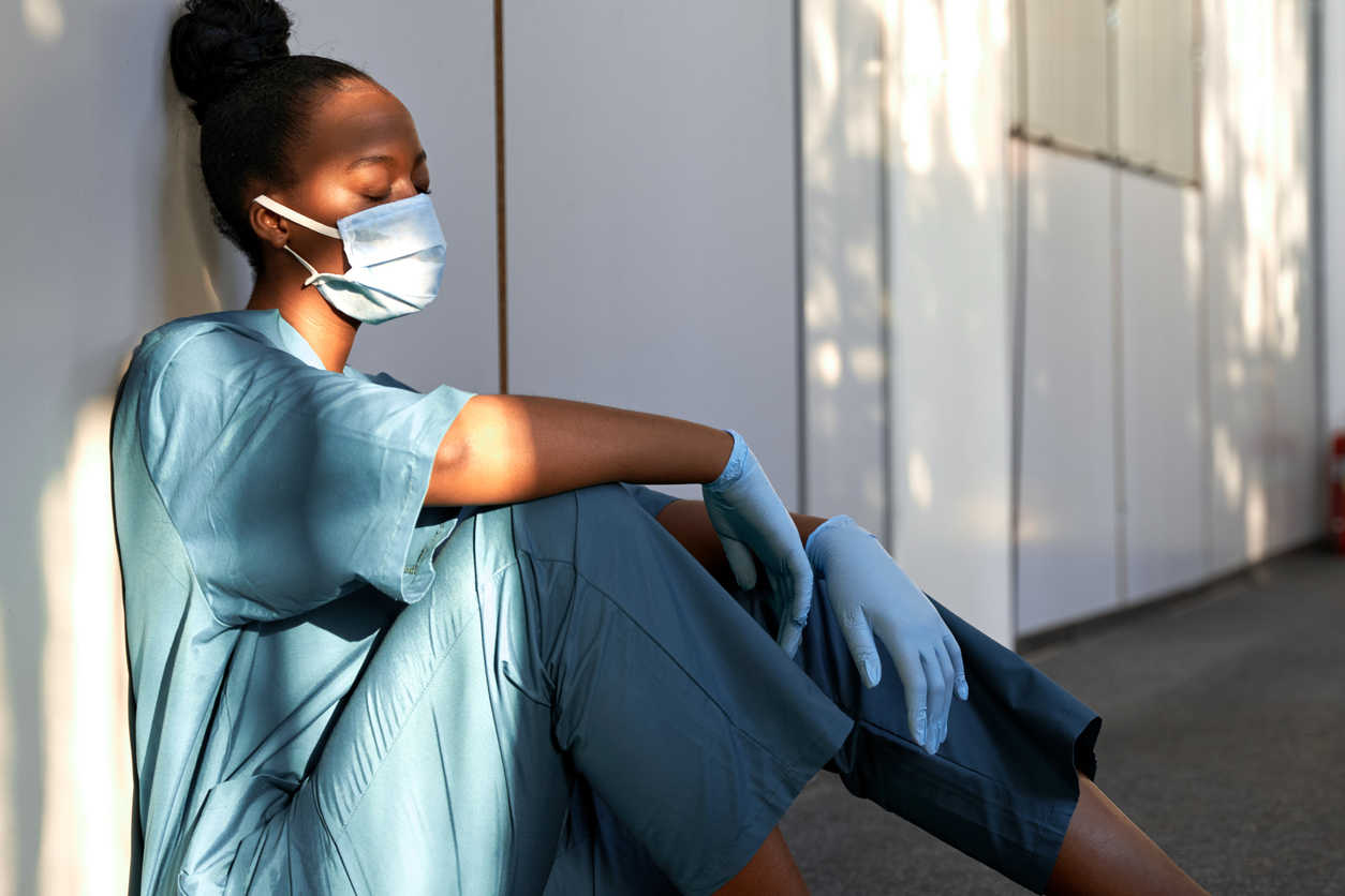 A nurse sits on hospital floor, overworked by Covid-related patients.
