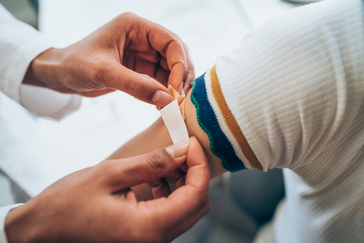 Female doctor putting a bandage on the arm of a female patient after administration a Covid-19 vaccine shot at a clinic.