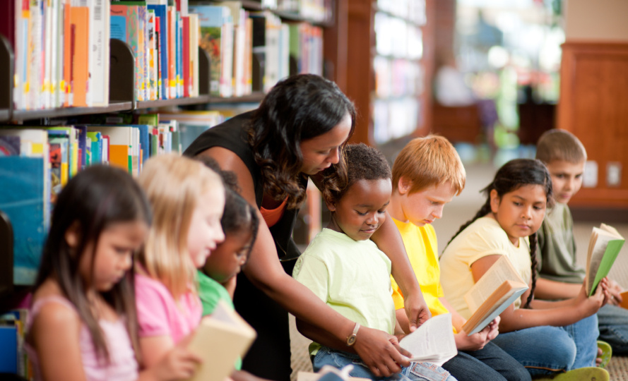 Diverse children in a library with their teacher
