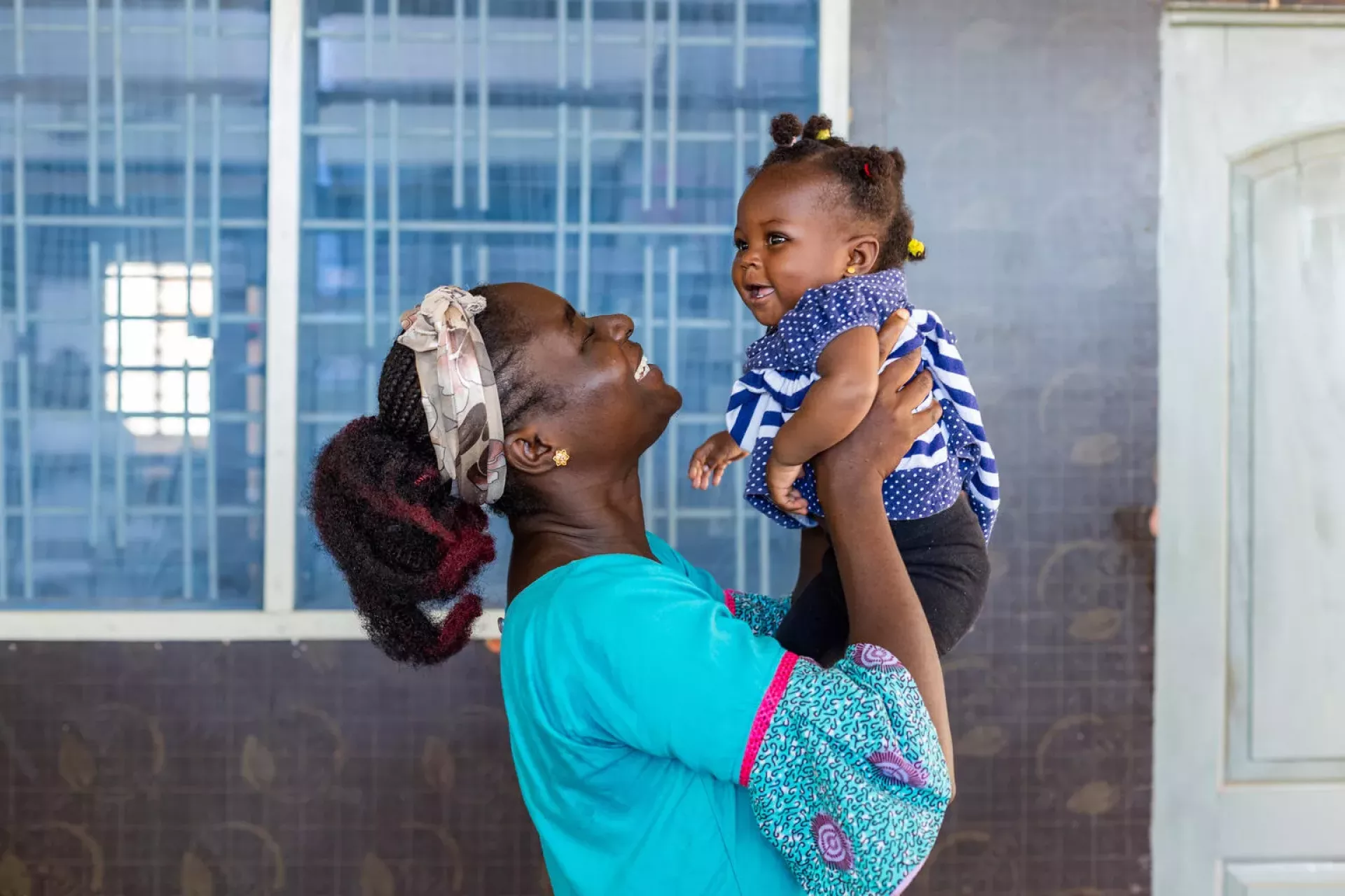 A Caribbean mother lifts her baby in a tender moment, reflecting the personal realities behind falling regional birth rates as women weigh the costs, support systems and long-term demands of motherhood.